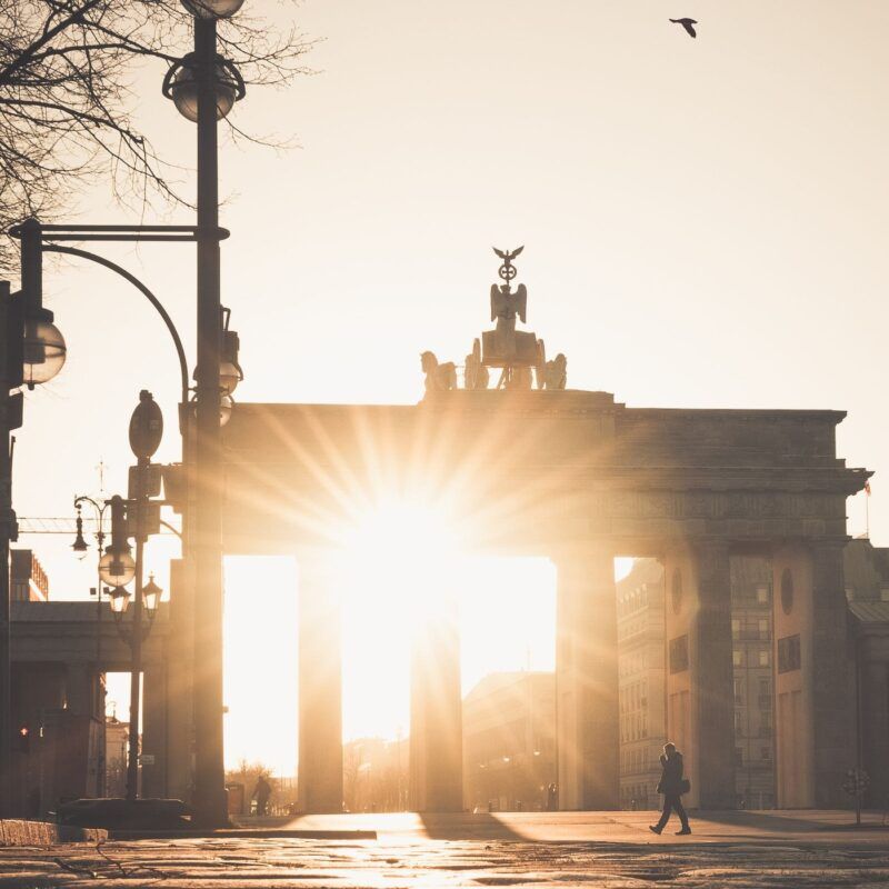 Das Brandenburger Tor im Gegenlicht der tiefstehenden Sonne, ein Passant geht vorbei