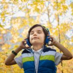 Junge mit Kopfhörern genießt Hörspiel im goldenen Herbstlaub